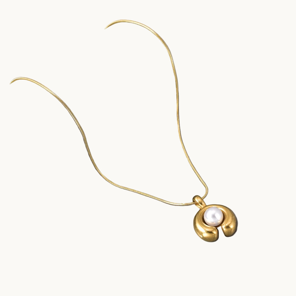 Gold necklace with a pearl pendant on a gray background
