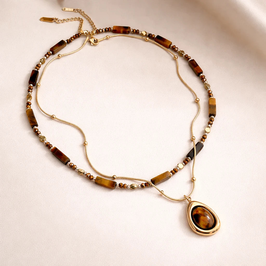 Necklace with gold chain and brown teardrop pendant on a beige background