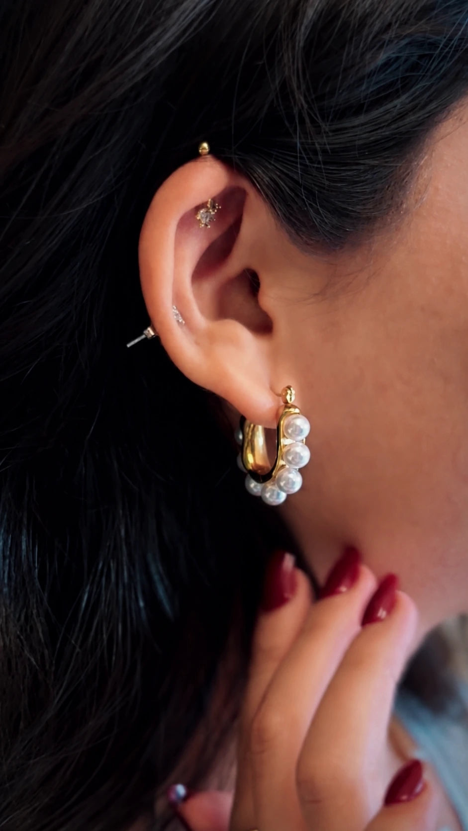 A close-up of a person's ear showcasing a gold hoop earring adorned with a row of white faux pearls, along with other ear piercings.