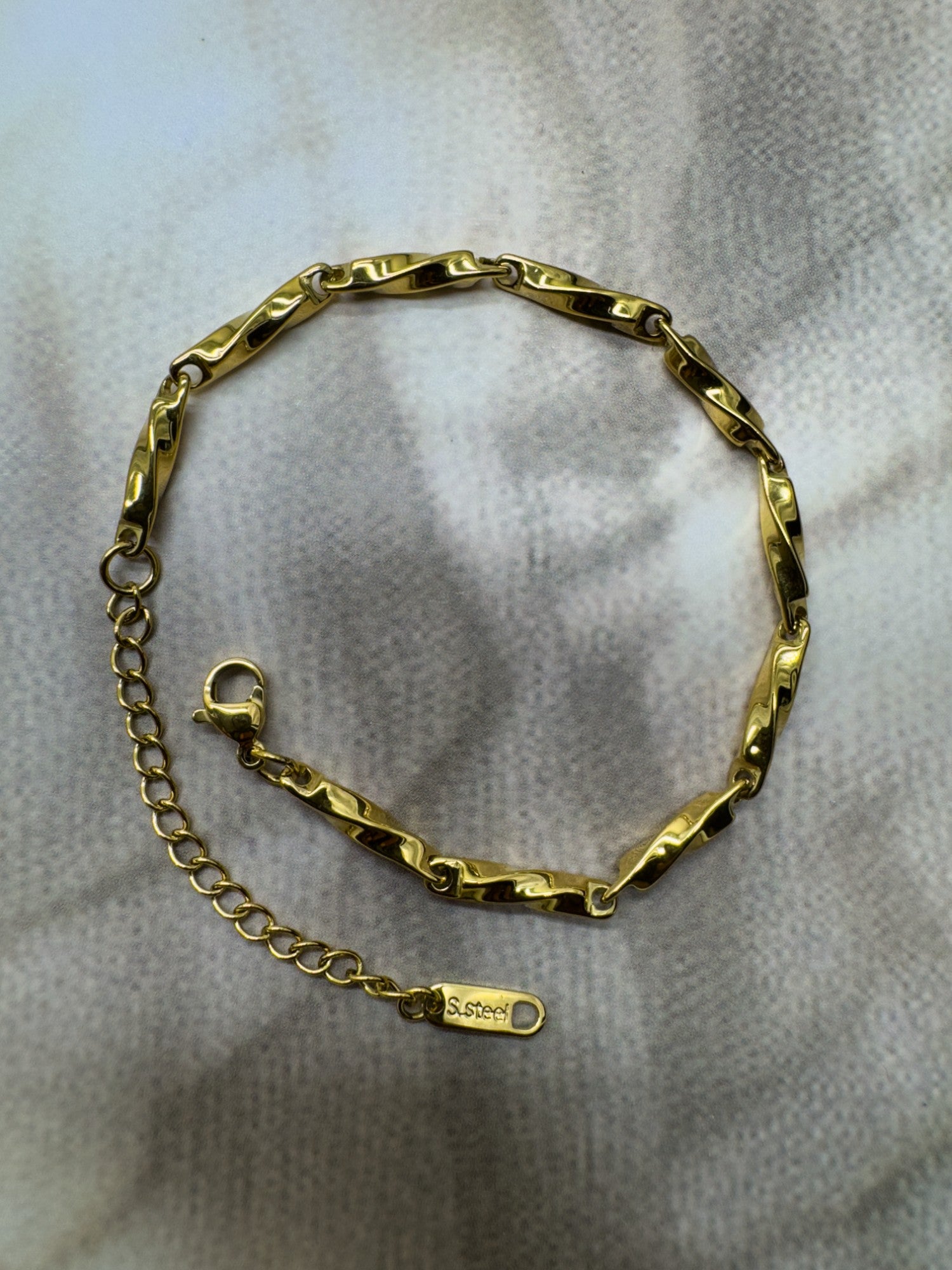 Gold chain bracelet on a light gray fabric background
