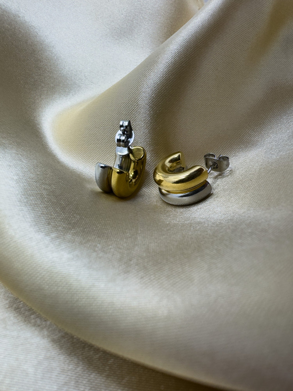 Pair of gold and silver snake-shaped earrings on a beige fabric background